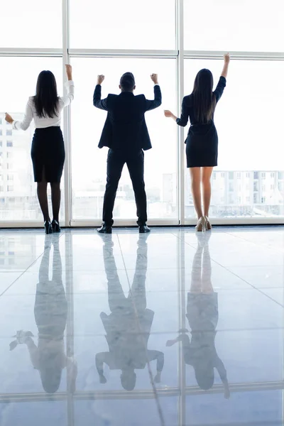 Business people raised hands in office team satisfied with result, won profitable contract, group of winners celebrate victory or great success against windows. — Stock Photo, Image