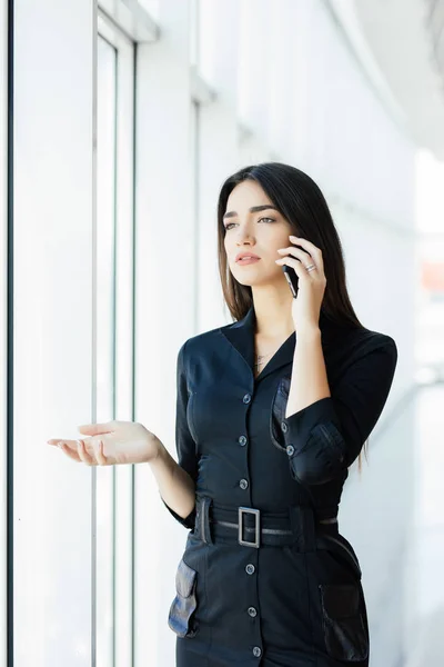 Portré, fiatal munkavállaló beszél, használ sejt telefon, nézett ki az ablakon. Női bíró üzleti hívás, elfoglalva a munkahelyen. — Stock Fotó