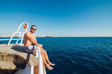 Genç yakışıklı adam denizde seyir yat kenarında oturan güneş gözlüğü