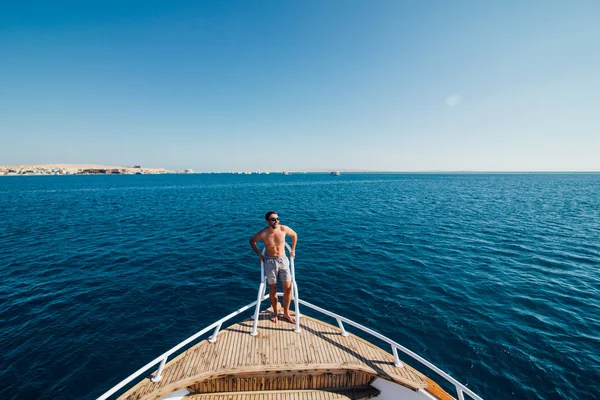Красивый человек, стоящий на палубе яхты и отдыхающий под солнцем в море — стоковое фото