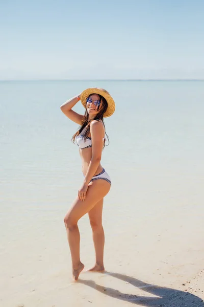 Donna felice sulla spiaggia in occhiali da sole e un cappello di paglia su acqua di mare blu — Foto Stock