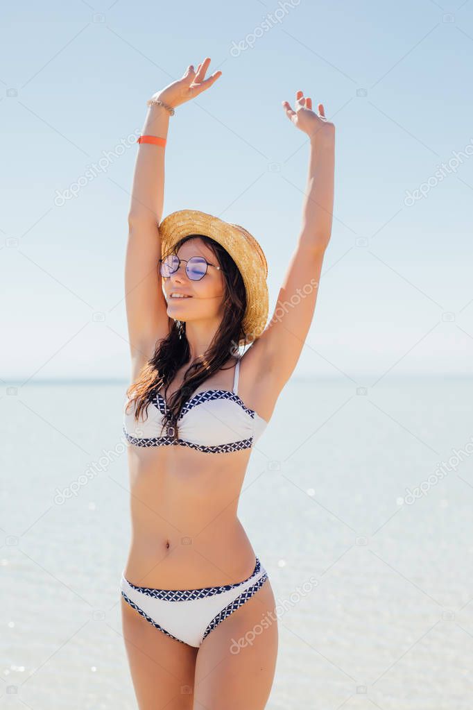 Attractive brunette in elegant white bikini looking at camera on a beautiful sunny sea beach