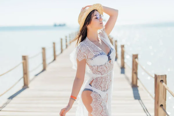 Ragazza posa al molo mare in cappello di paglia e occhiali da sole. Donna in costume da bagno sexy sulla spiaggia tropicale sul cielo blu sole. Vacanze estive. Ricreazione, attività, concetto di svago . — Foto Stock