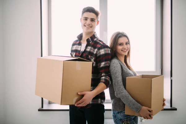 Par med lådor som flyttar in i nya hem leende. Ungt par på flyttdagen. — Stockfoto