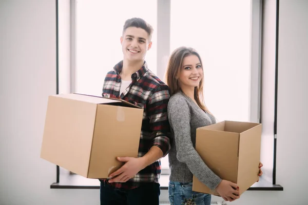Par med lådor som flyttar in i nya hem leende. Ungt par på flyttdagen. — Stockfoto