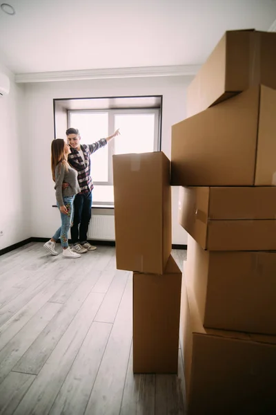 Linda pareja mirando por la ventana en su nuevo hogar. feliz pareja mudándose casa sentado cerca de ventana con completo boxex habitación —  Fotos de Stock