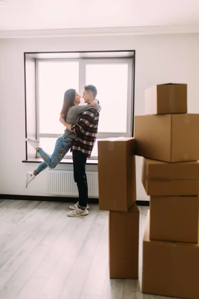 Casal jovem bem sucedido está se movendo para novo lugar agradável e abraçando, ao redor são caixas de papelão . — Fotografia de Stock