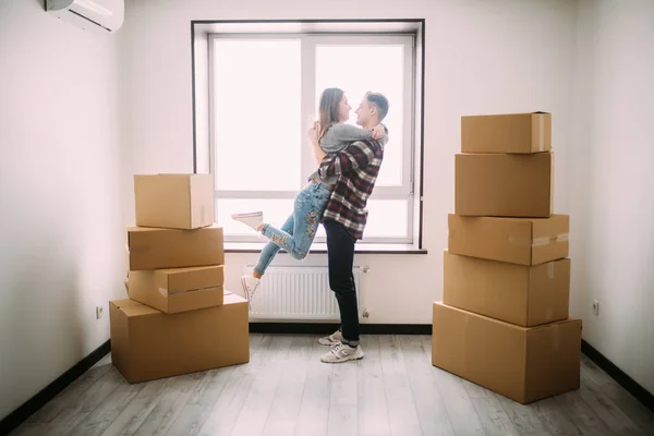 美丽的年轻夫妇的全长肖像拥抱和微笑, 而站在移动纸板箱在空房间里 — 图库照片