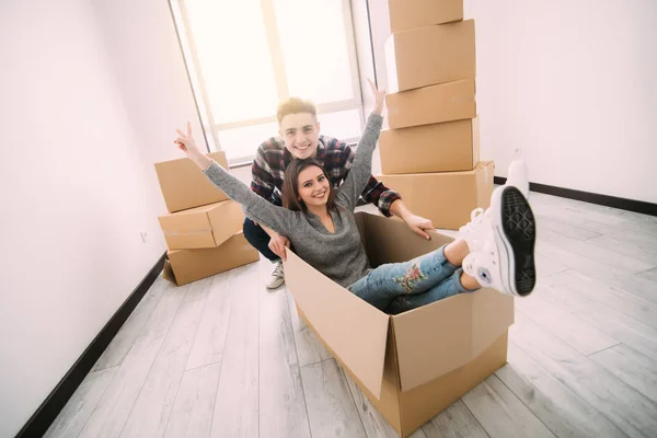 Feliz jovem casal está se divertindo com caixas de papelão em nova casa no dia em movimento . — Fotografia de Stock