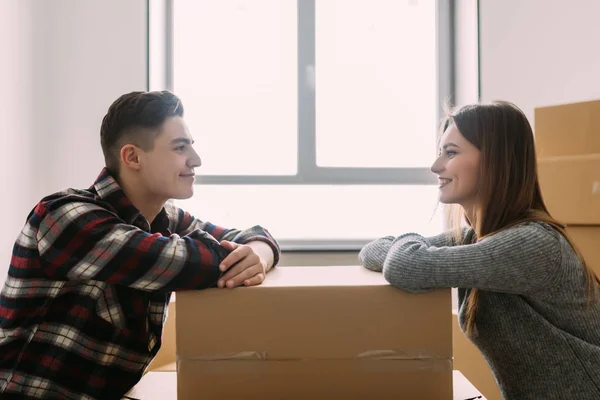 Unga lyckliga paret flyttar hus ser varandra lutande på en låda — Stockfoto