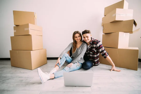 Unga par som flyttar nya hem sitter på golvet och avkopplande efter uppackning ser något på laptop. Omlokalisering — Stockfoto