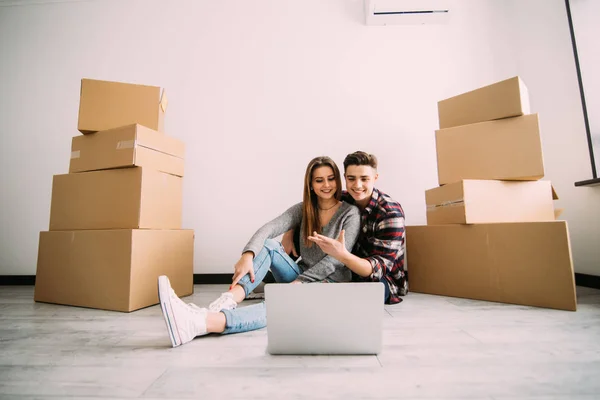 Unga par som flyttar nya hem sitter på golvet och avkopplande efter uppackning ser något på laptop. Omlokalisering — Stockfoto