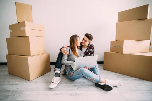 Pareja joven enamorada sentada en el suelo de su nuevo apartamento, planeando la redecoración y la búsqueda de ideas en un ordenador portátil — Foto de Stock