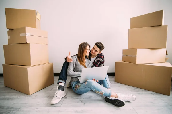 Unga par som flyttar i ett nytt hem. Man och kvinna med rutorna i tomma rum och bärbar bärbar dator. — Stockfoto