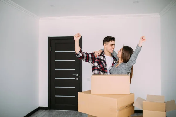 Glad och lycklig ung par seger höjde händerna på sitt nya hem med rörliga kartong under flytta in i ny lägenhet — Stockfoto