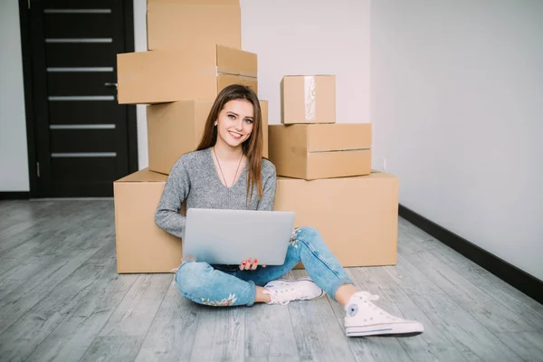 Ung kvinna rör sig i en lägenhet, sitter på golvet och surfa på nätet på laptop på jakt efter nya inredningsidéer. — Stockfoto