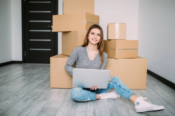 Glad ung kvinna flytta till nya hem sitter på golvet och använda laptop nära lådor — Stockfoto