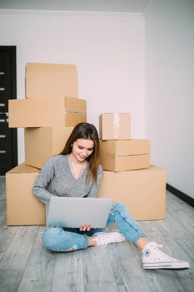 Ung kvinna rör sig i en lägenhet, sitter på golvet och surfa på nätet på laptop på jakt efter nya inredningsidéer. — Stockfoto