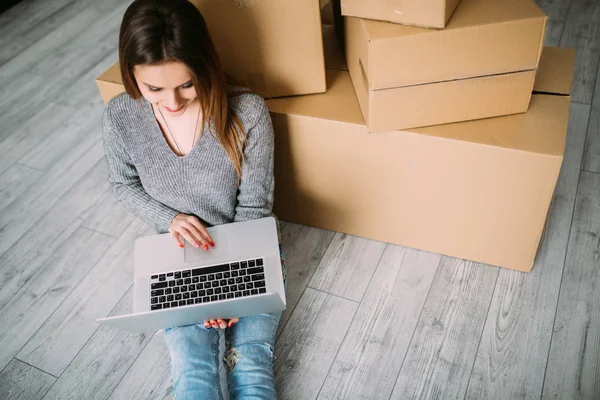 Kvinna sitter på golvet nära en lådor med laptop medan du flyttar till nya hause — Stockfoto
