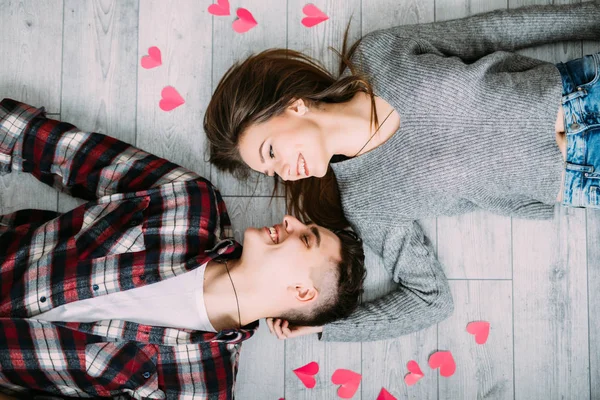 年轻可爱的夫妇躺在灰色的木地板上, 红色的心从上面看. — 图库照片