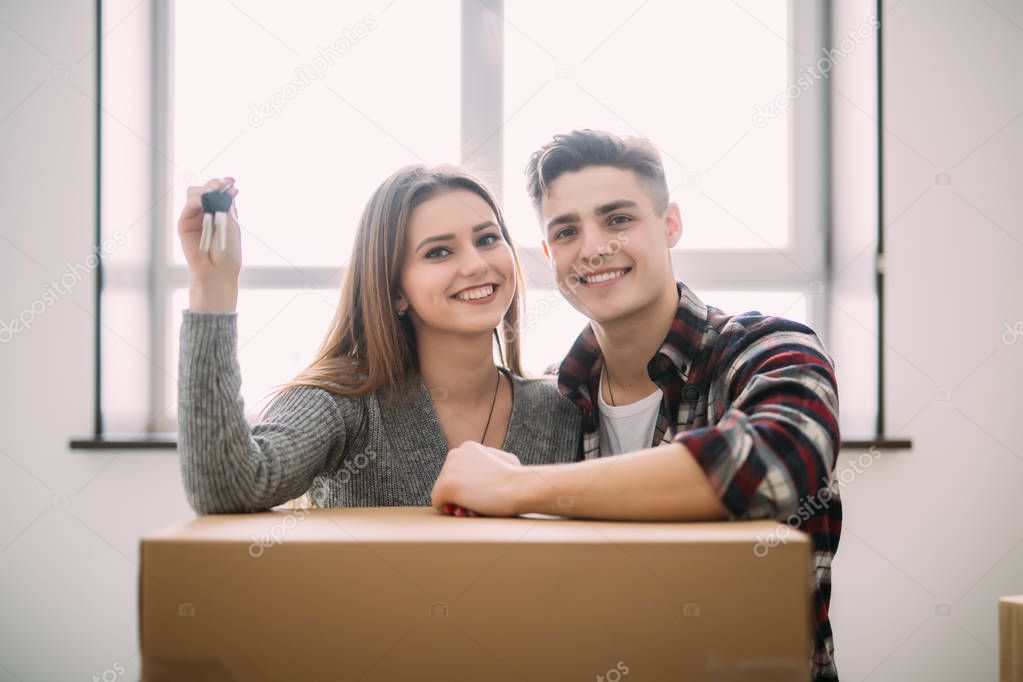 Young smile couple sit on the floor around boxes holding key in hand