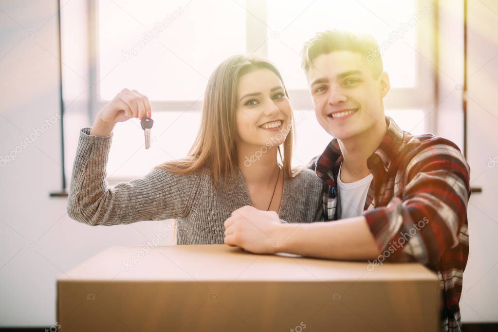 Young smile couple sit on the floor around boxes holding key in hand