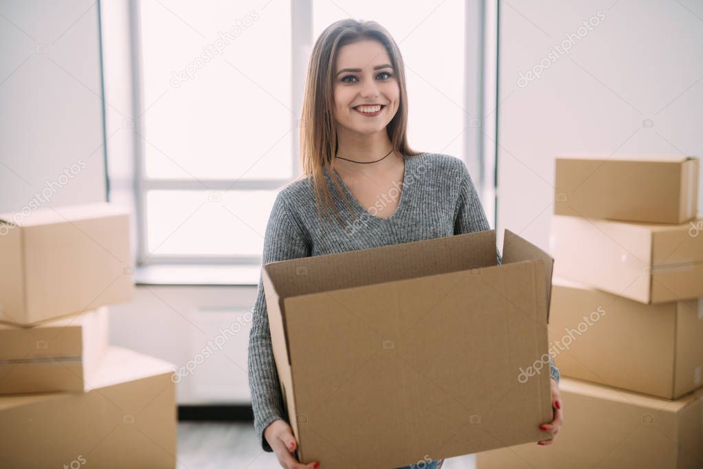 Portrait of beautiful young brunette packing carrying some boxes to move into her new home