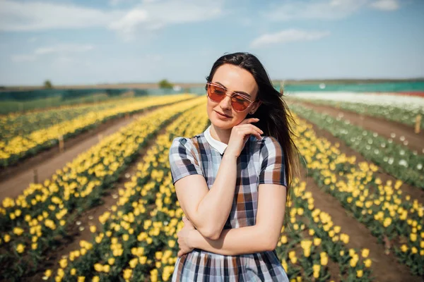 Giovane bella donna con occhiali da sole in un giardino con un sacco di tulipani gialli — Foto Stock