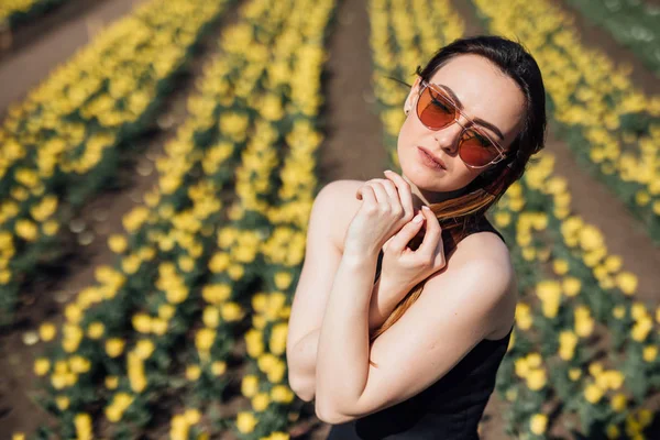 Fiatal nő szépségét napszemüveg, fekete ruha tulipán mező kertben — Stock Fotó