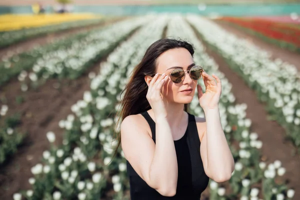 Giovane donna in occhiali da sole in Primavera giornata di sole su tulipani campo di fiori. Festa della mamma. Primavera — Foto Stock