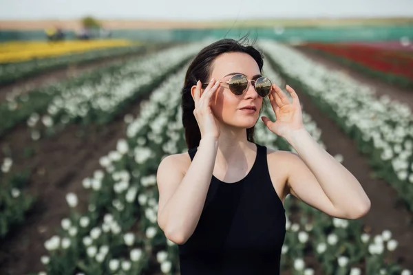 Giovane donna in occhiali da sole in Primavera giornata di sole su tulipani campo di fiori. Festa della mamma. Primavera — Foto Stock