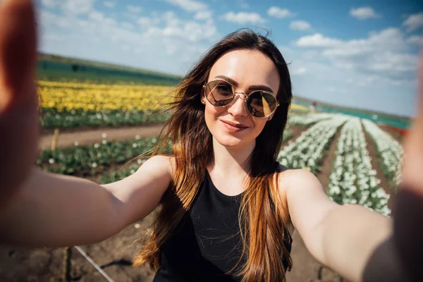 Giovane bella donna indossare occhiali da sole fare selfie nel campo di fiori tulipani nella soleggiata giornata primaverile — Foto Stock