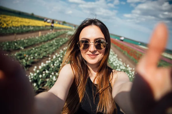 Giovane bella donna indossare occhiali da sole fare selfie nel campo di fiori tulipani nella soleggiata giornata primaverile — Foto Stock