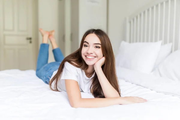 Hermosa mujer joven mirando a la cámara mientras está acostada en la cama en casa —  Fotos de Stock