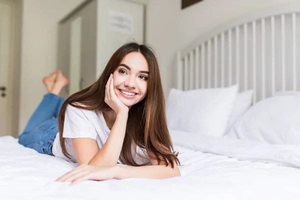 Mujer joven acostada en su cama mira hacia adelante y una mano sobre su mejilla . —  Fotos de Stock