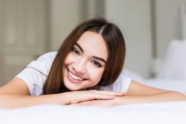 Молода щаслива жінка лежить на білому ліжку і посміхається вдома — стокове фото