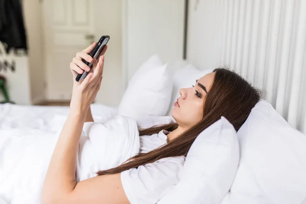 Расслабленная молодая женщина дома читает смс в своей светлой спальне — стоковое фото