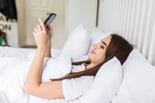 Расслабленная молодая женщина дома читает смс в своей светлой спальне — стоковое фото