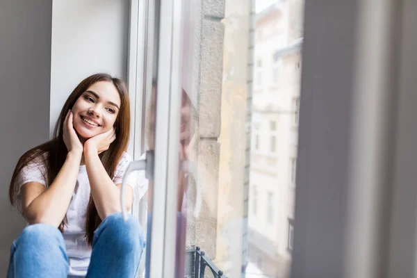 Beautiful smiling woman sitting on windowsill — Stock Photo, Image