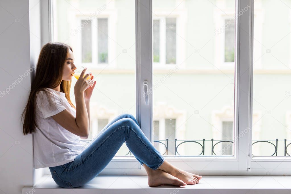 Smiling woman with glass of juice sitting on windowsill