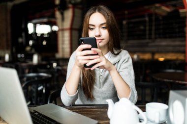 Genç kadın ya da kahve dükkanı iç akıllı telefon ve dizüstü bilgisayara başarılı çalışma. Teknoloji kullanırken Üniversitesi kafeteryada oturan kız öğrenci.