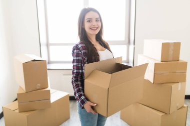 Genç kadın karton yığını içinde onun yeni hause kutuları mutlu, kameraya gülümsüyor
