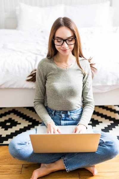 Hermosa joven mujer que trabaja desde casa en un ordenador portátil sentado en el suelo en la habitación . — Foto de Stock