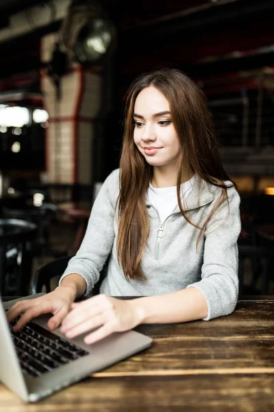 食堂使用のノート パソコンに座ってコーヒーを飲みながらフリーランスの若い女性 — ストック写真