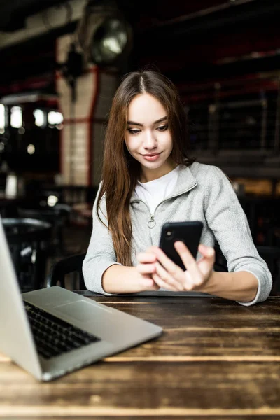 女性モダンなカフェでスマート フォンのメッセージ書き込みの入力。コーヒーまたはカプチーノの携帯電話を使用してテーブルに座って若いきれいな女の子の画像をトリミング. — ストック写真