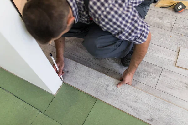 Mužské pracovní instalaci laminátových podlah, muž instalace nové dřevěné laminátové podlahy. Muž pokládání laminátové podlahy doma. Carpenter pracovník instalaci laminátové podlahy v místnosti — Stock fotografie