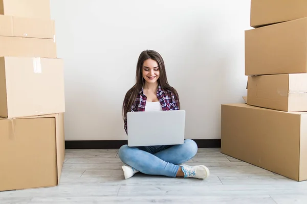 Ung kvinna rör sig i en lägenhet, sitter på golvet runt lådor och surfa på nätet på en bärbar dator på jakt efter nya inredningsidéer. — Stockfoto
