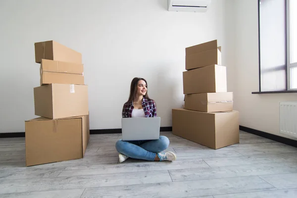 Ung kvinna rör sig i en lägenhet, sitter på golvet runt lådor och surfa på nätet på en bärbar dator på jakt efter nya inredningsidéer. — Stockfoto