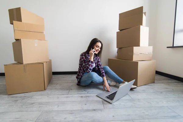 Ung kvinna som sitter på golvet nära en lådor med laptop — Stockfoto