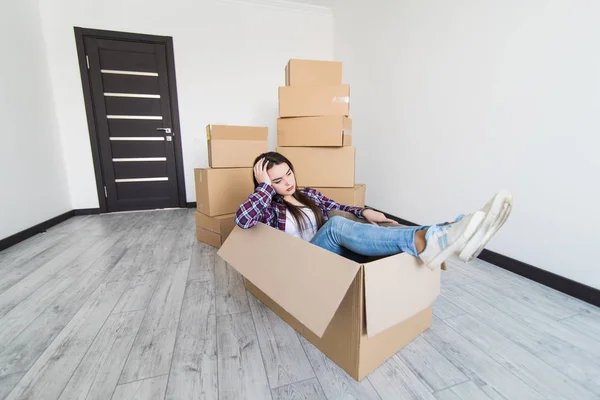 Cheerful sad and tired woman sitting in a cardboard box white moving in new appartmant — Stock Photo, Image